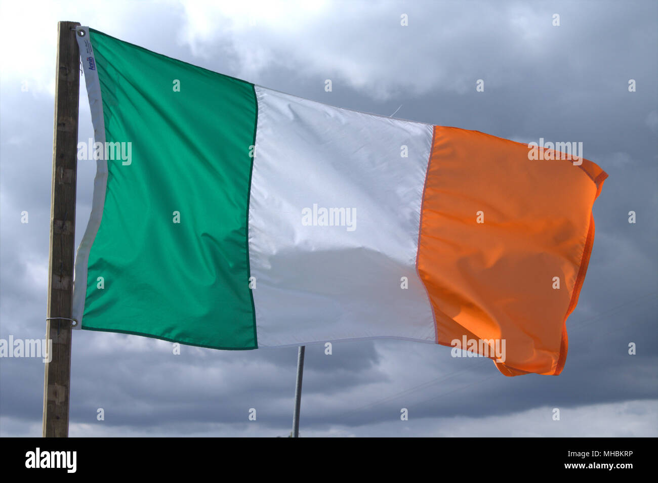 Irlanda bandiera nazionale tricolore e alfiere della Repubblica di Irlanda volare in un vento rigido contro un cielo tempestoso. Foto Stock