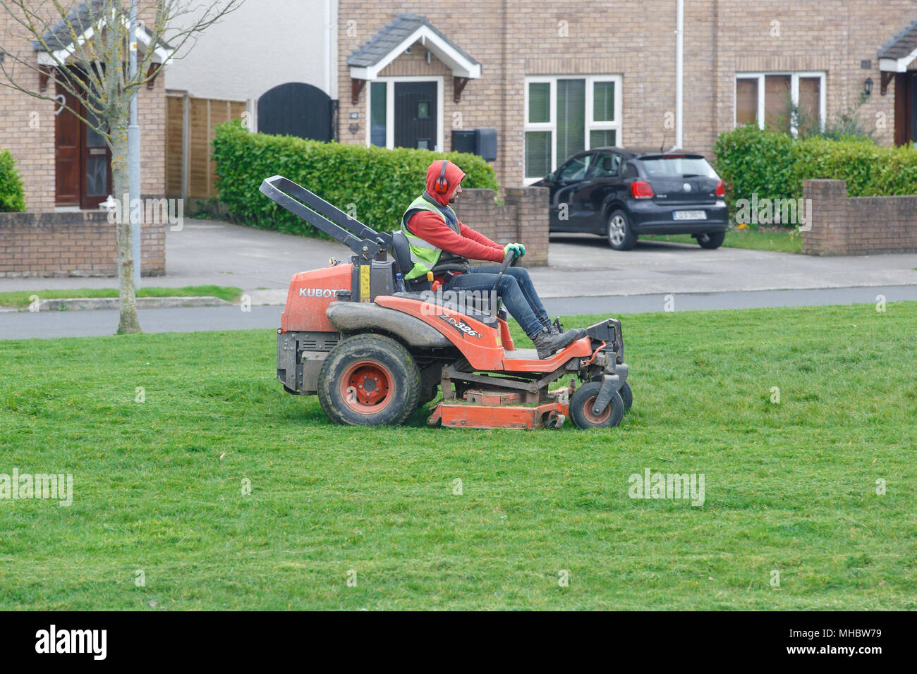 Uomo in cuffie di protezione commerciale di equitazione tosaerba uno verde in estate. Cura del prato. Molla di manutenzione all'aperto. Erba Foto Stock