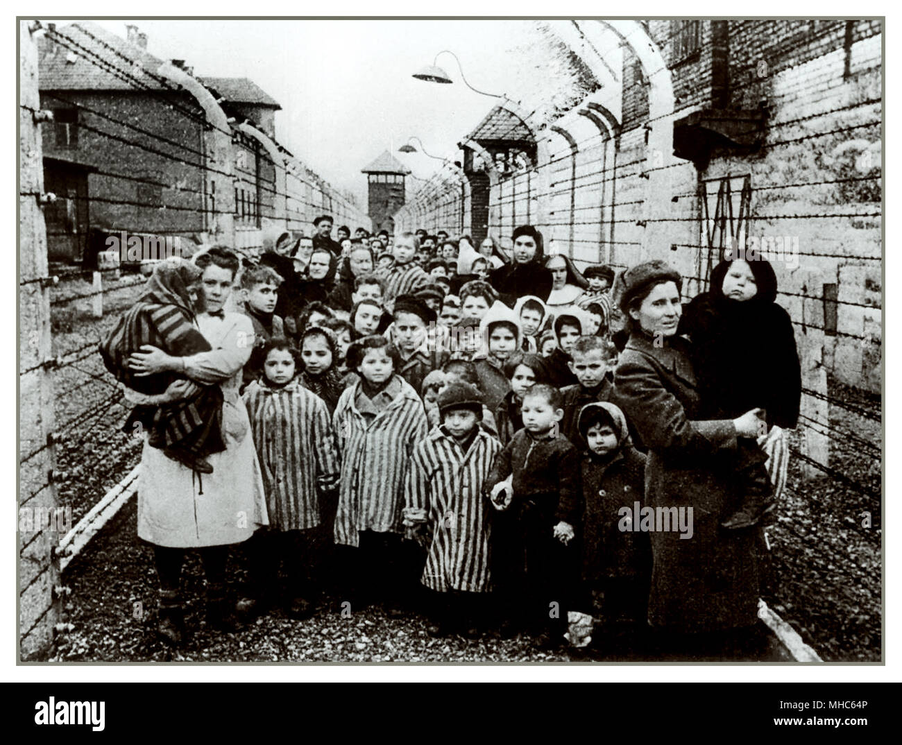 AUSCHWITZ BAMBINI SOPRAVVISSUTI DETENUTI NEONATI E DONNE UNIFORMI DA CAMPO A STRISCE LIBERAZIONE chiusa da tratti di filo spinato elettrificato e posti di guardia, che fissano senza emozione i loro liberatori. Un'altra cornice di orrore dal campo di concentramento nazista di Auschwitz Birkenau. Data di liberazione: Gennaio 27 1945. Foto Stock