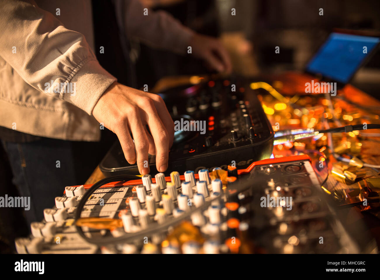 Chiusura del giovane DJ di riproduzione di musica in club alla moda, concentrarsi sulle mani su DG miscelatore con illuminato di luci, spazio di copia Foto Stock