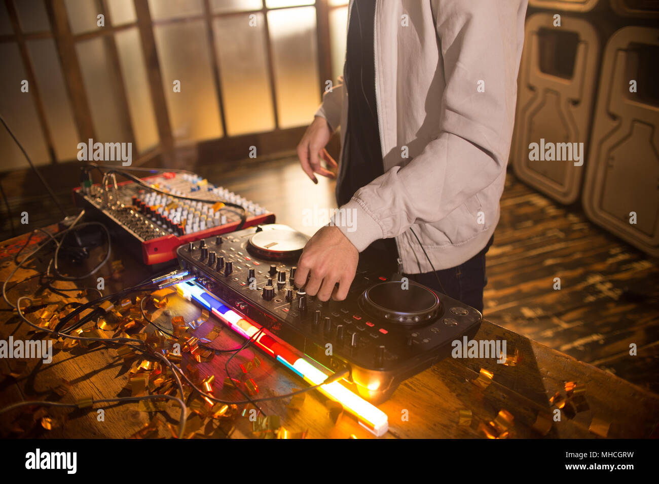 Angolo alto close up del giovane DJ di riproduzione di musica in club alla moda, concentrarsi sulle mani su DG miscelatore con illuminato di luci, spazio di copia Foto Stock
