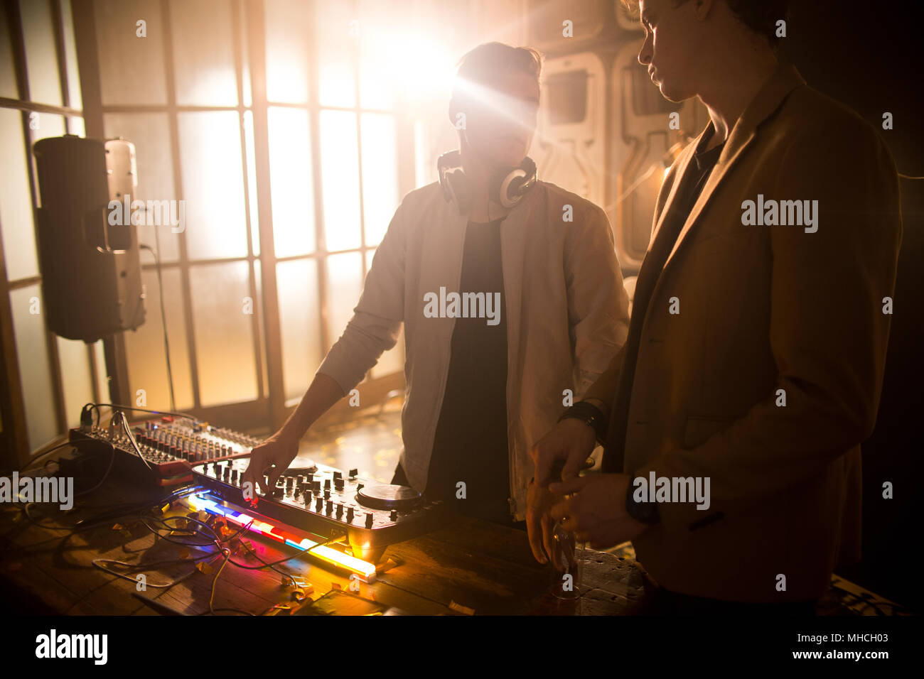Backlit Ritratto di giovane DJ permanente al mixer rendendo la musica durante la festa notturna in club e parlando a ventole Foto Stock