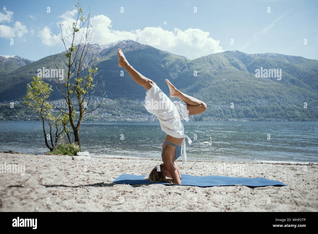 Giovane donna esercizio di yoga in riva al lago e montagne, girato in Canton Ticino, Svizzera, Europa. Persone relax benessere concept Foto Stock