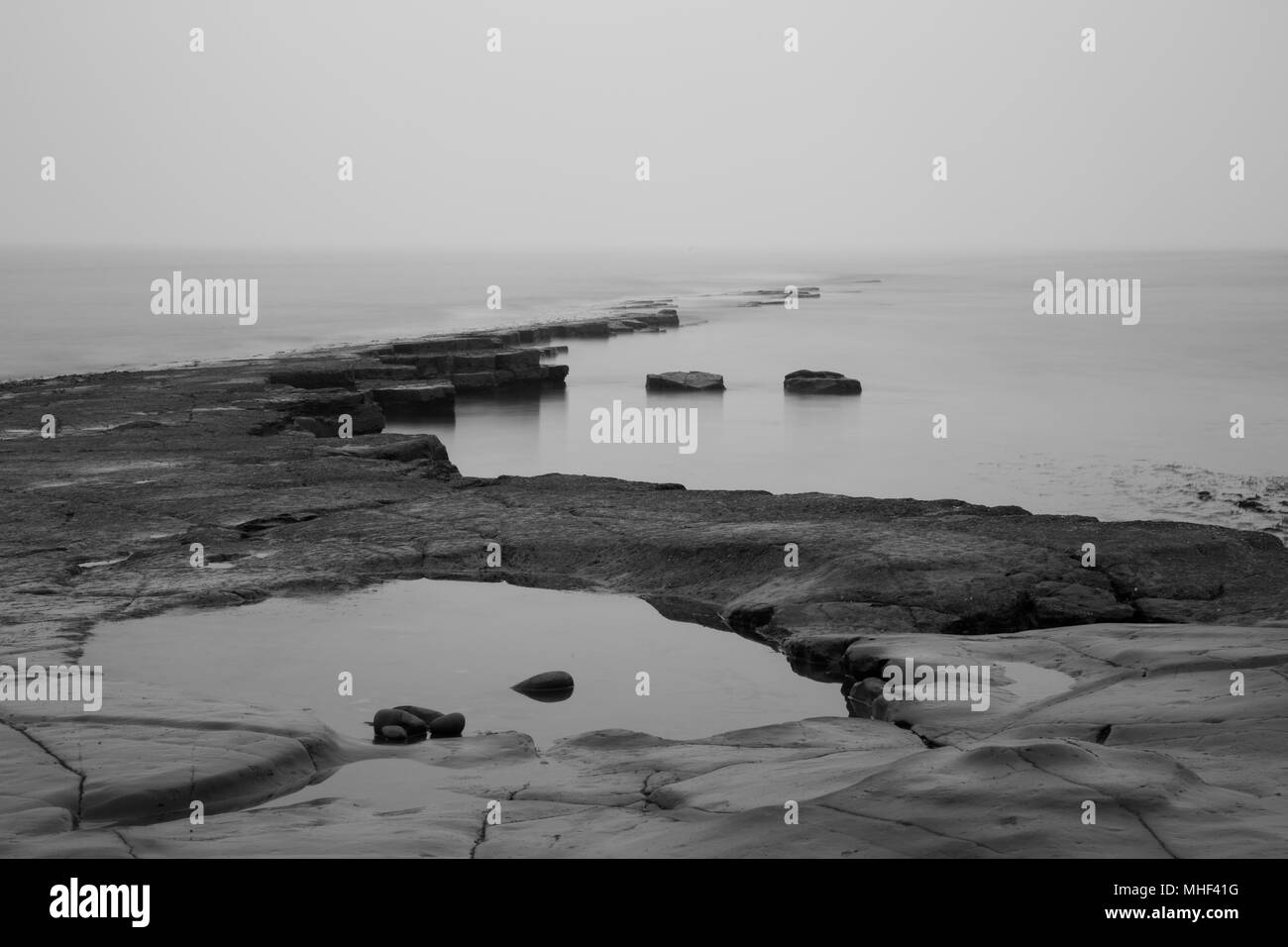 Pavimentazione Kimmeridge, rocce sporgenti al mare in una nebbiosa mattina. calma foto Foto Stock