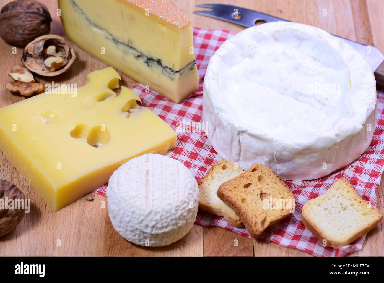 Formaggio francese platter - Camembert, Morbier, Emmental e formaggio di capra su rosso in stile country tovagliolo e tavola di legno. Foto Stock