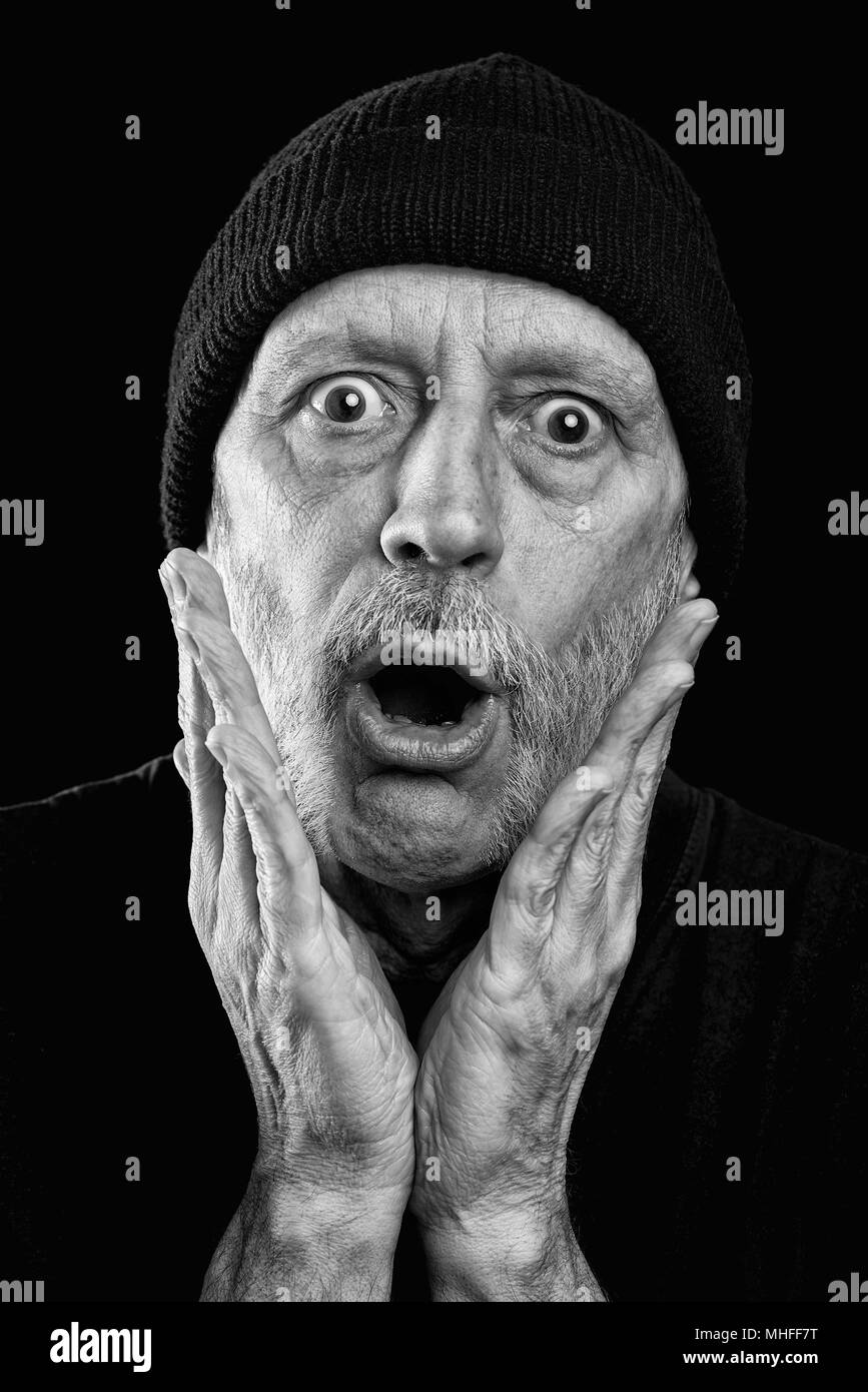 Drammatica foto in bianco e nero di una sorpresa o paura uomo forte con la barba con un tappo di lana sulla testa, mettendo le mani sul suo volto Foto Stock