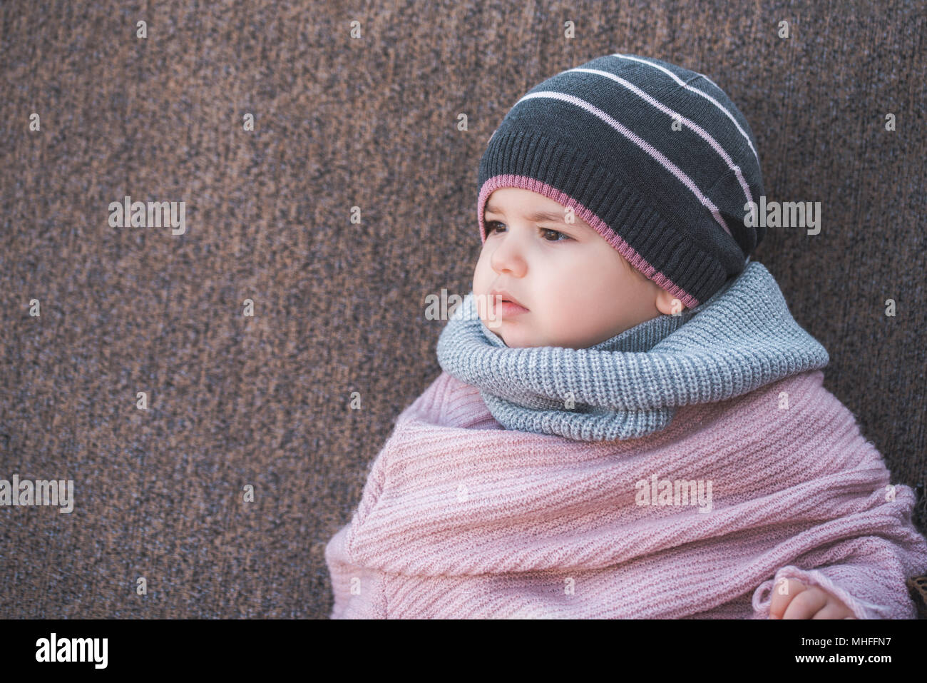 Carino bambina indossa un caldo inverno cappello e una sciarpa colorata su uno sfondo marrone Foto Stock