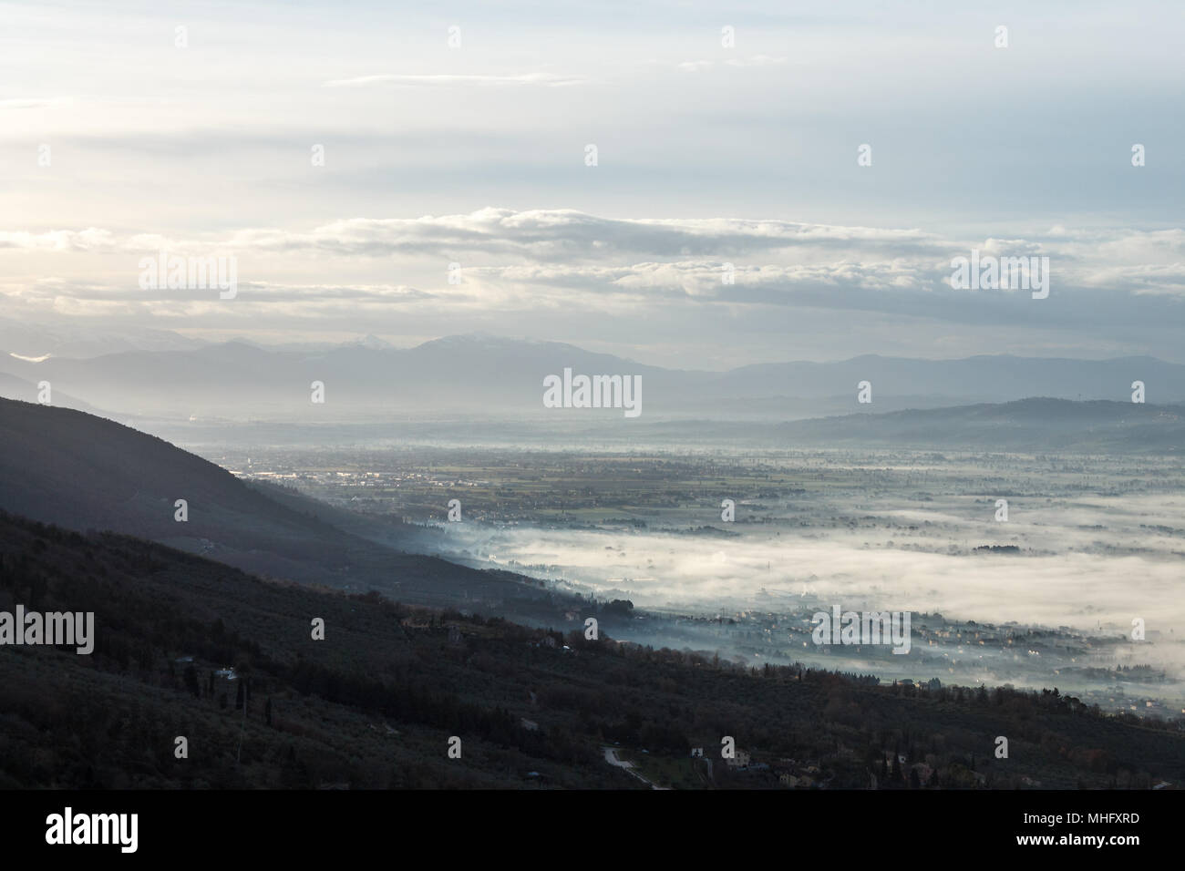 Splendida vista della valle umbra in un inverno mattina, con la nebbia che copre gli alberi e le case Foto Stock