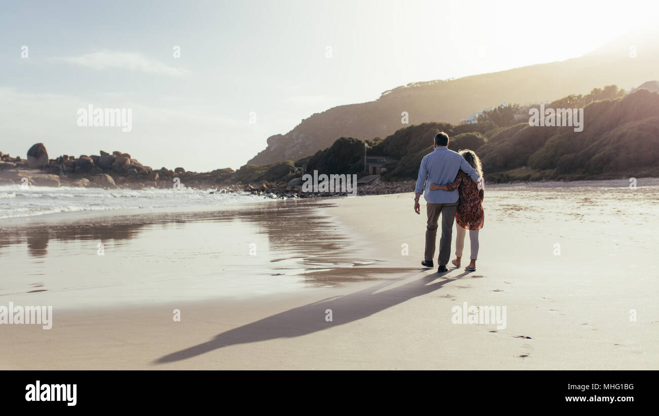 Coppia matura a piedi con bracci intorno sulla spiaggia di mattina. Amorevole Coppia matura avente una passeggiata sulla riva del mare. Foto Stock