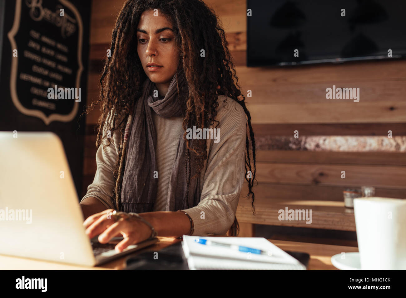 Donna seduta presso un ristorante tabella lavorando sul computer portatile. Libero professionista in seduta cafe con un caffè, blocco note e penna funzionante sul computer portatile. Foto Stock