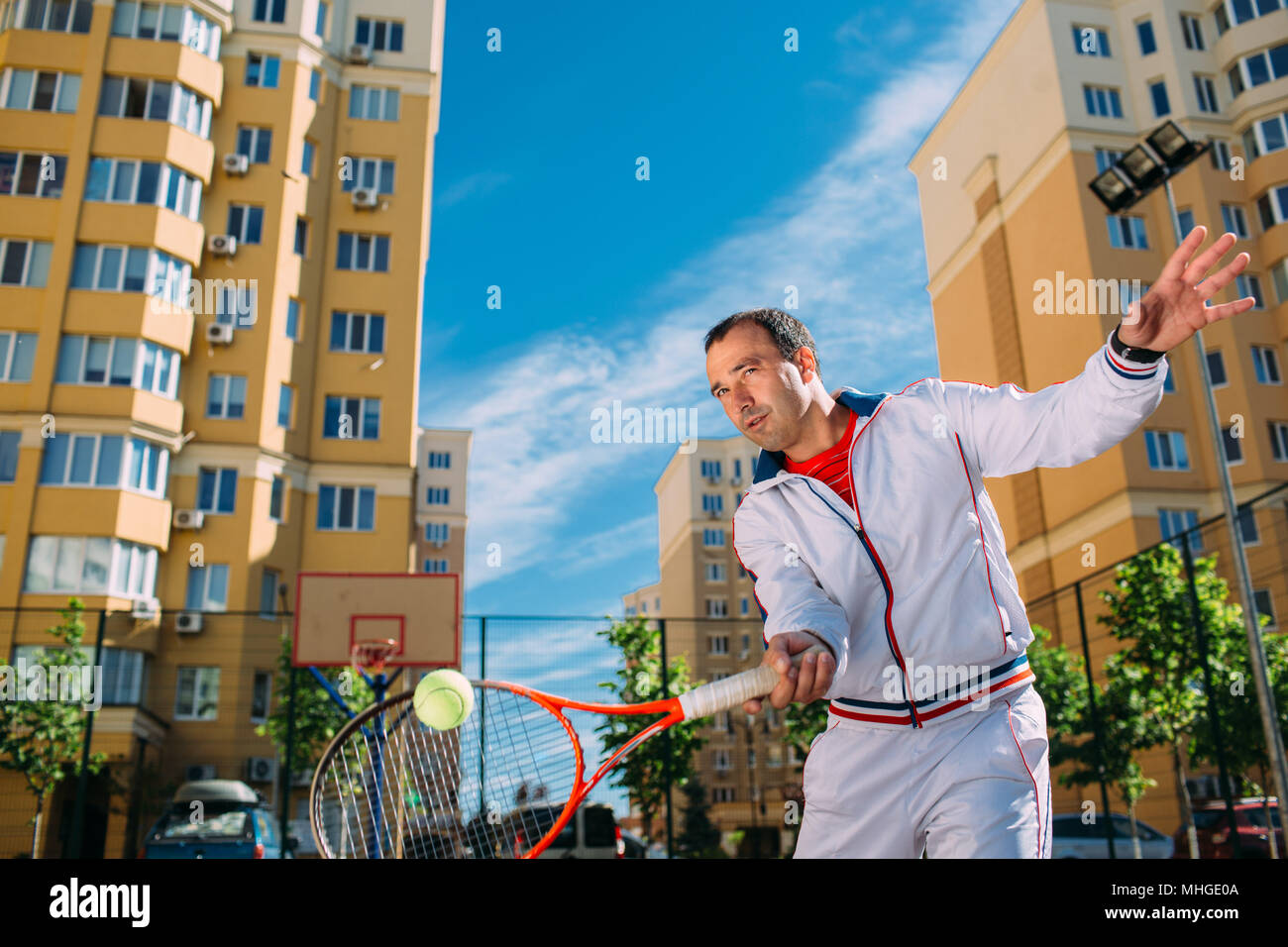 Determinato bello tennista giocare a tennis e a colpire la palla, sul soleggiato Campo da tennis, a sfondo della città Foto Stock