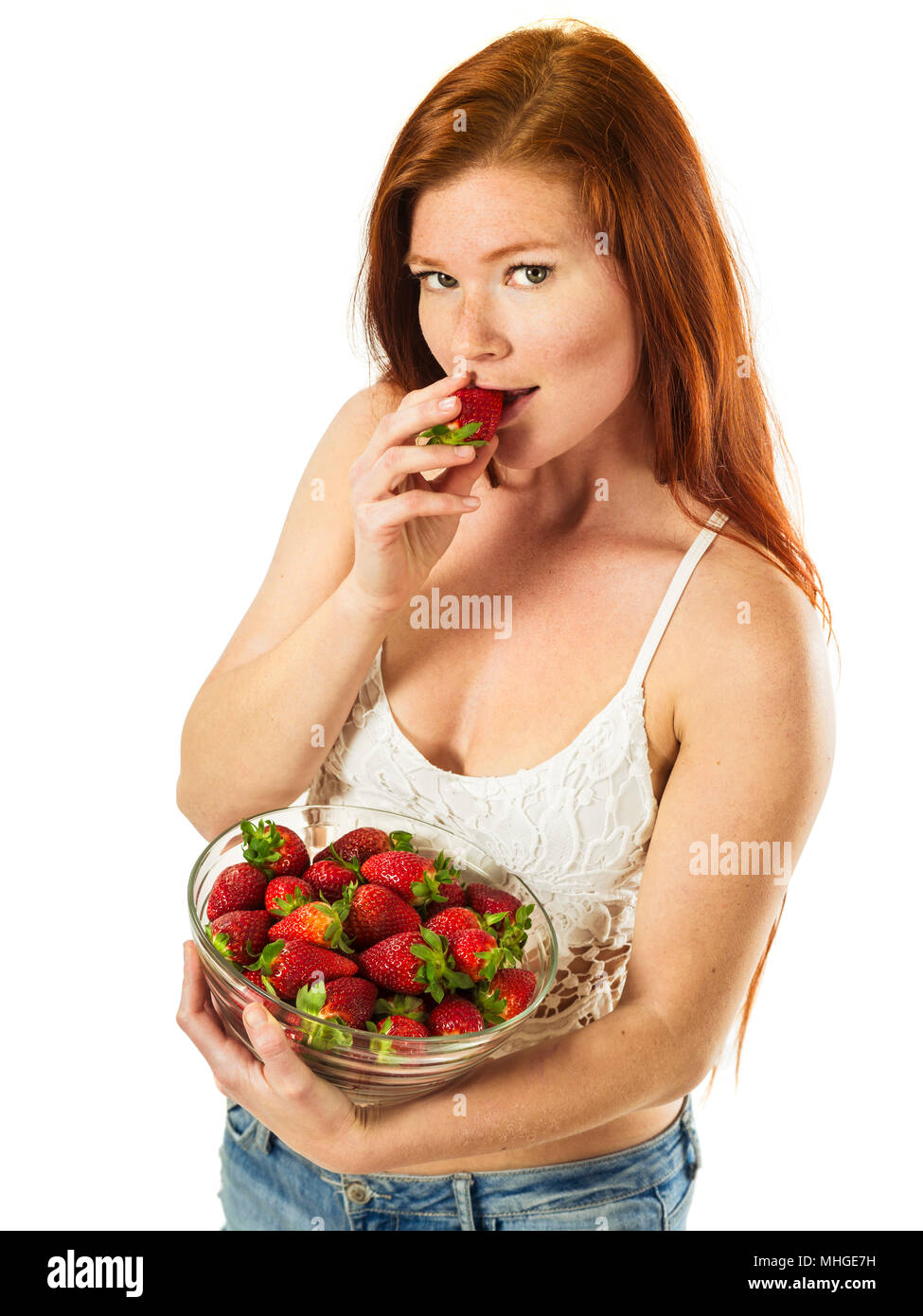 Foto di una bellissima giovane donna con lunghi capelli rossi tenendo una tazza di fragole su sfondo bianco. Foto Stock