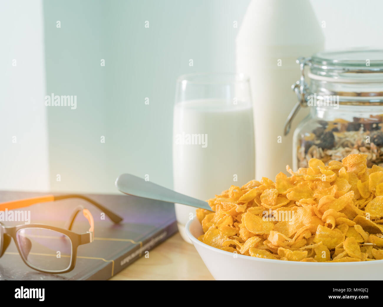 Ciotola di cereale con cucchiaio e un bicchiere di latte mettere sul tavolo di legno vicino a diabete textbook e occhiali. Cibo di calcio prima colazione . Cornflakes e latte Foto Stock