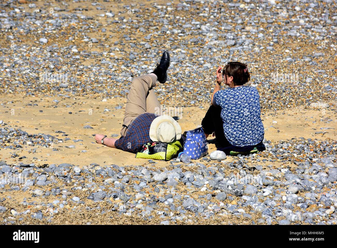 Coppia di mezza età rilassante sulla spiaggia di ciottoli di CROMER Inghilterra NORFOLK REGNO UNITO Foto Stock