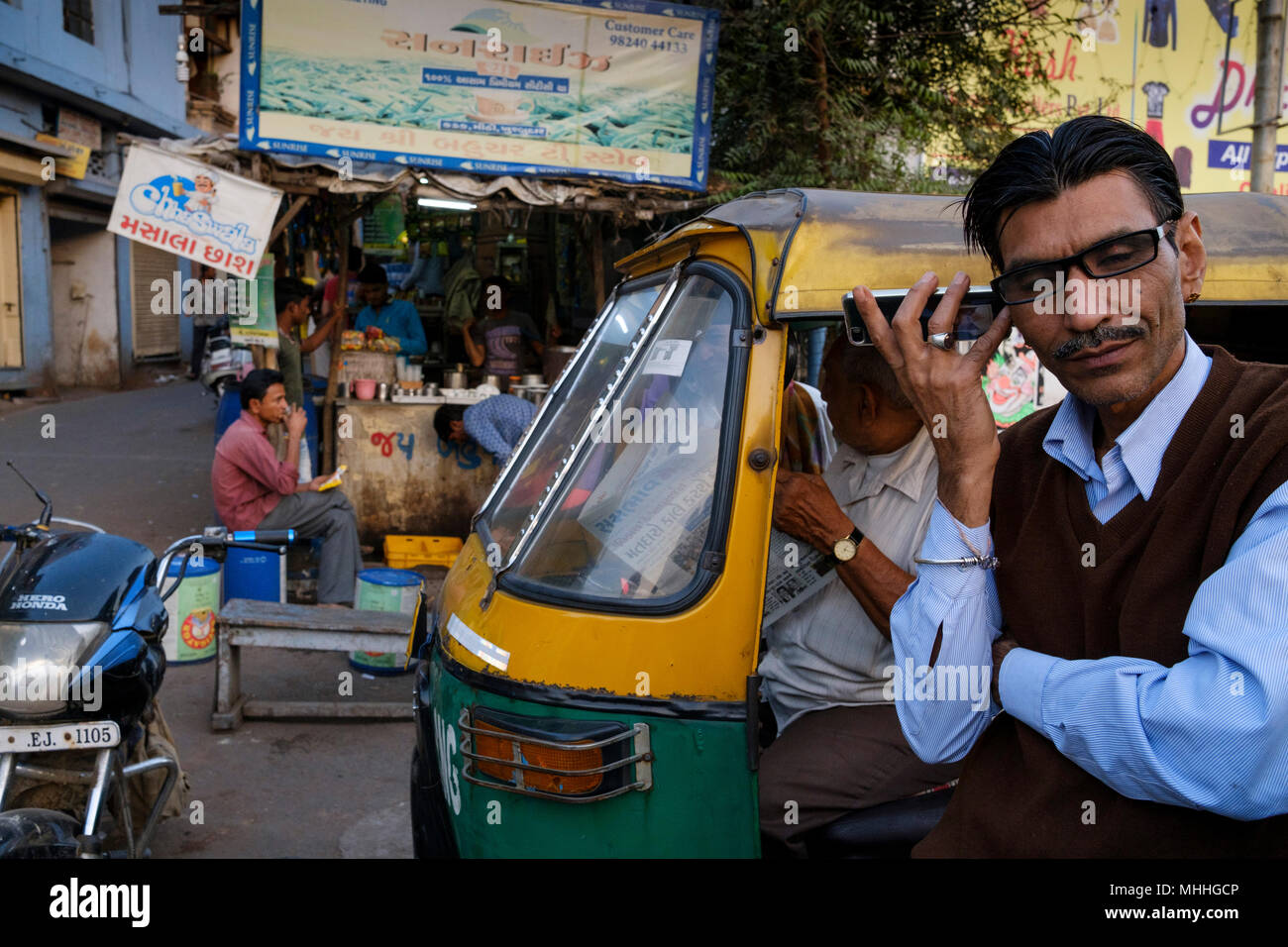 Uomo al telefono nella parte anteriore di un tuk tuk. La strada dello shopping di strade affollate nella parte vecchia della città di Ahmedabad, Manek Chowk. Foto Stock