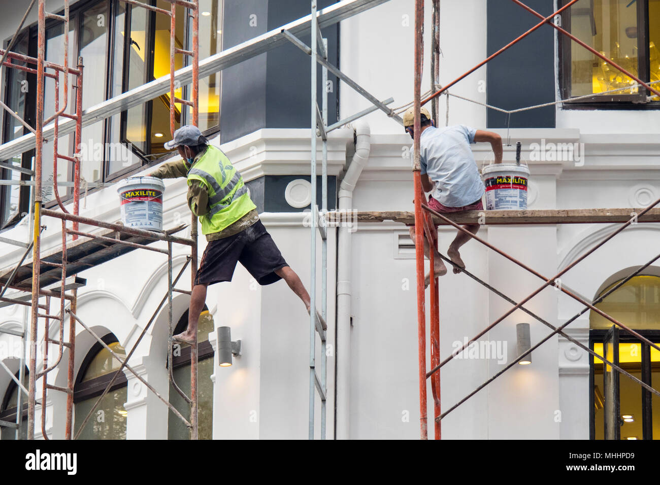 Due uomini su una impalcatura a lavorare in condizioni non sicure della pittura francese di un edificio in stile coloniale nel distretto 1, Ho Chi Minh City, Vietnam. Foto Stock