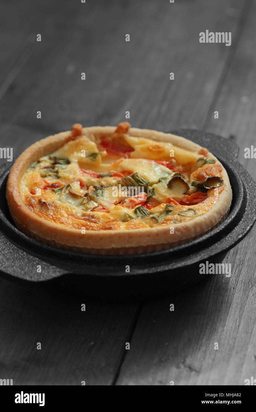 Pomodoro e cipolline quiche in una ghisa sottovaso su un sfondo di legno con colore selettivo Foto Stock