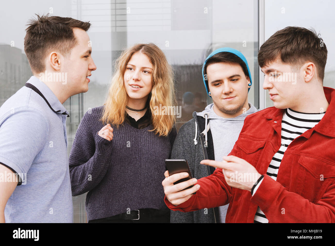 Gruppo di amici adolescenti avente una conversazione o discussione, giovane uomo è mostrando qualcosa sul suo smartphone Foto Stock