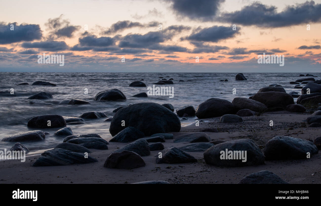Un paesaggio marino all'alba con grandi pietre scure su una spiaggia deserta vicino Kaltene, Lettonia. Foto Stock