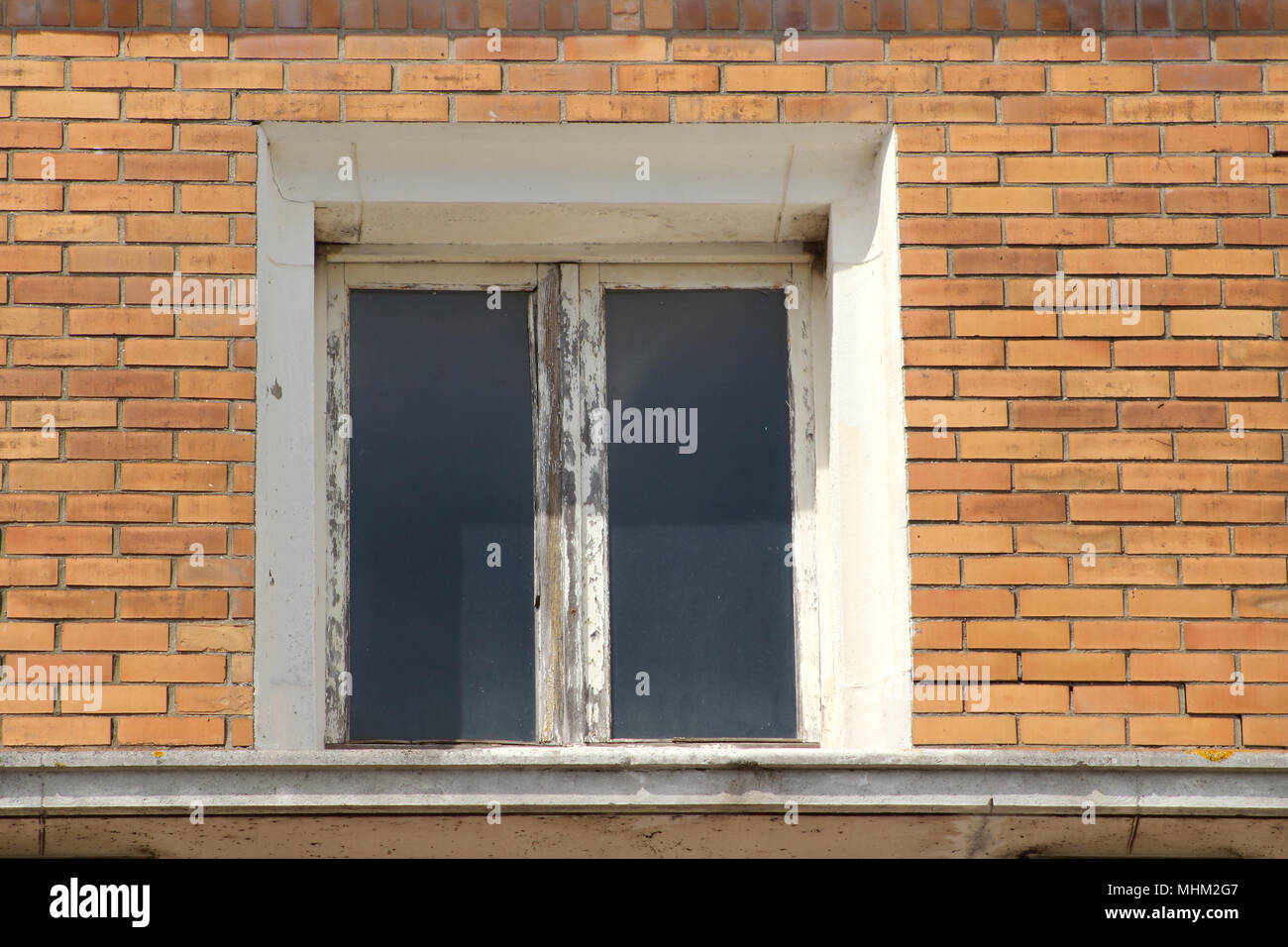 Una vecchia finestra con telaio in legno che necessita di un rinnovo su una casa di mattoni Foto Stock