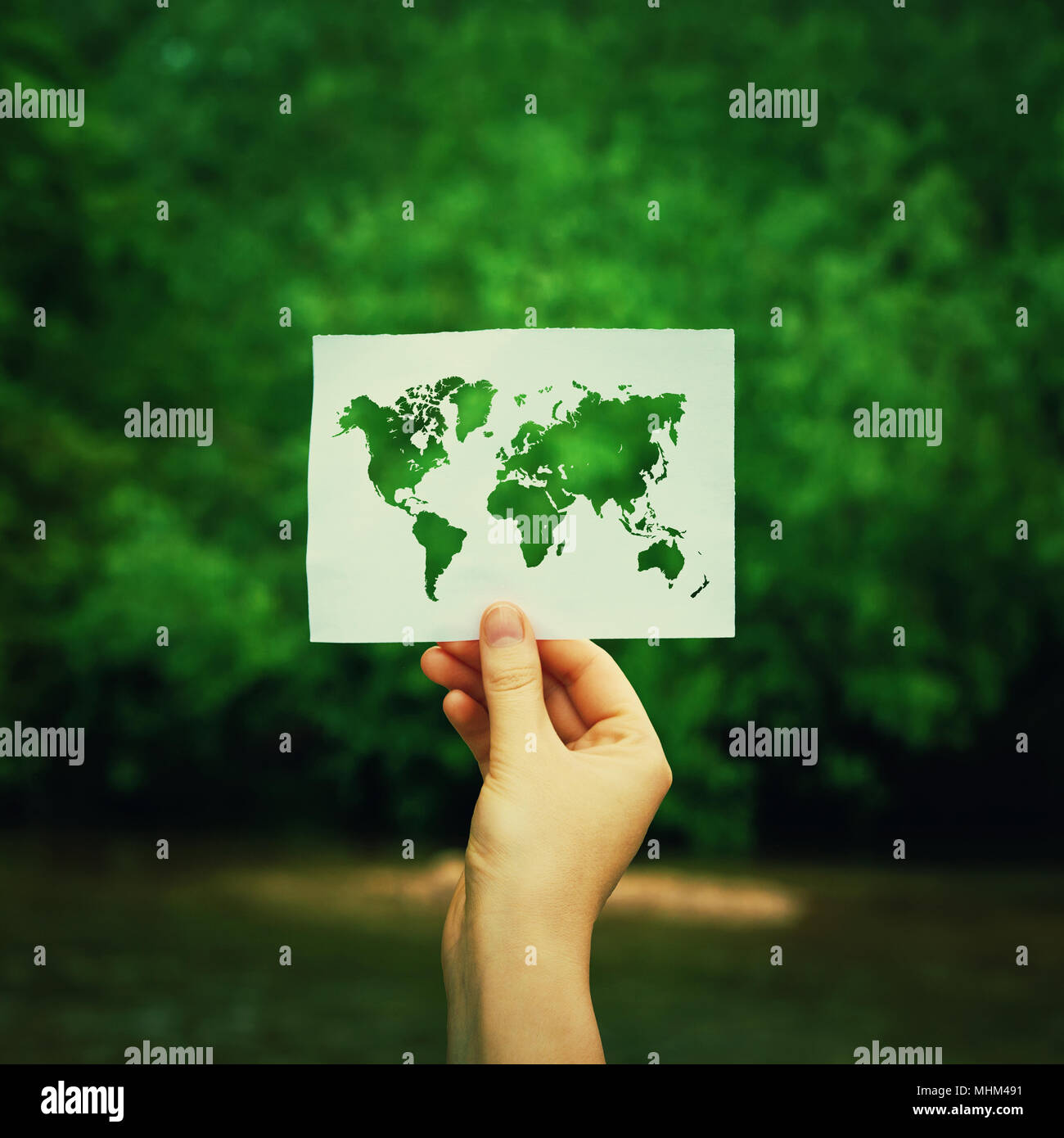 Donna mano tenendo un foglio di carta con la mappa del mondo sulla foresta verde natura dello sfondo. Ecologia e concetto di inverdimento, questioni ambientali globali wor Foto Stock