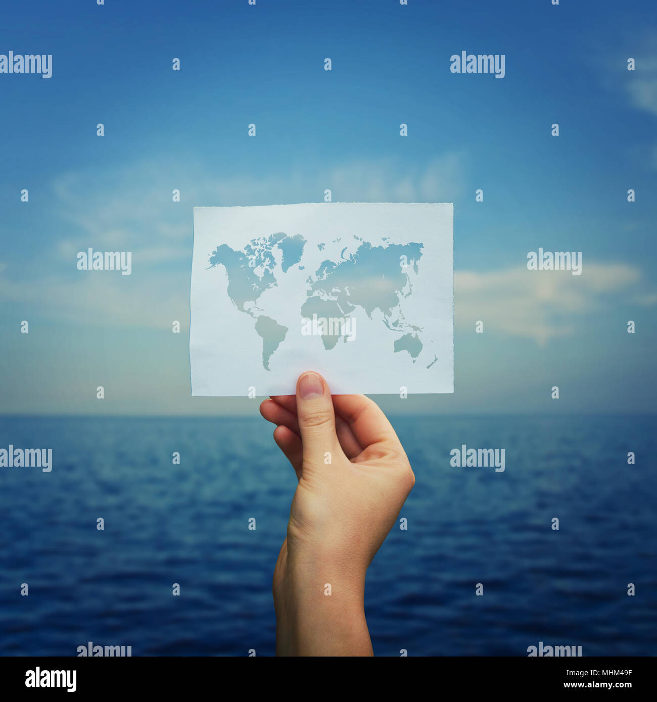 Donna mano tenendo un foglio di carta con la mappa del mondo oltre oceano blu sullo sfondo della natura. Viaggi di lavoro e vacanze estive. Foto Stock