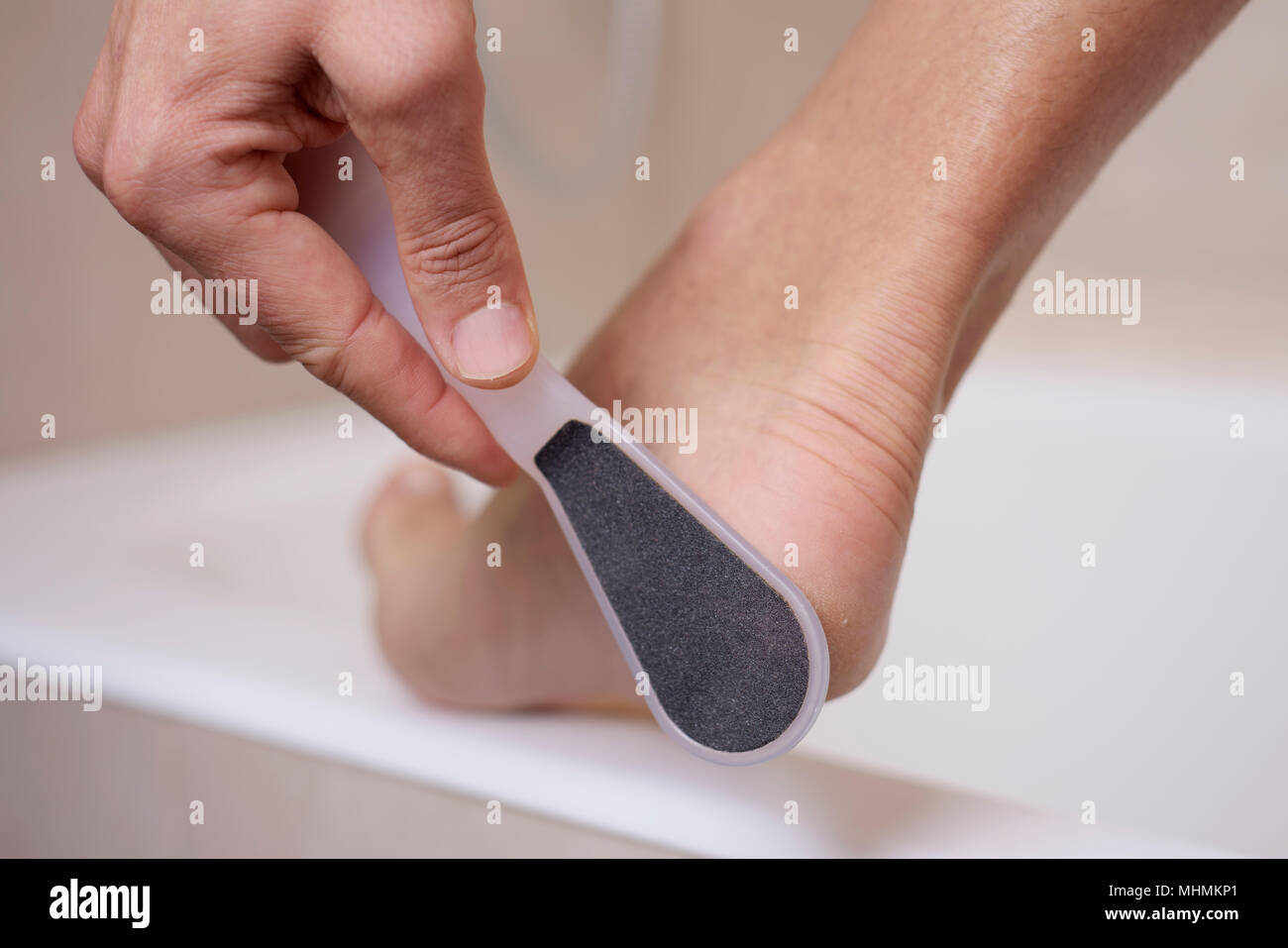 Primo piano di un giovane uomo caucasico in bagno utilizzando una raspa per piedi Foto Stock