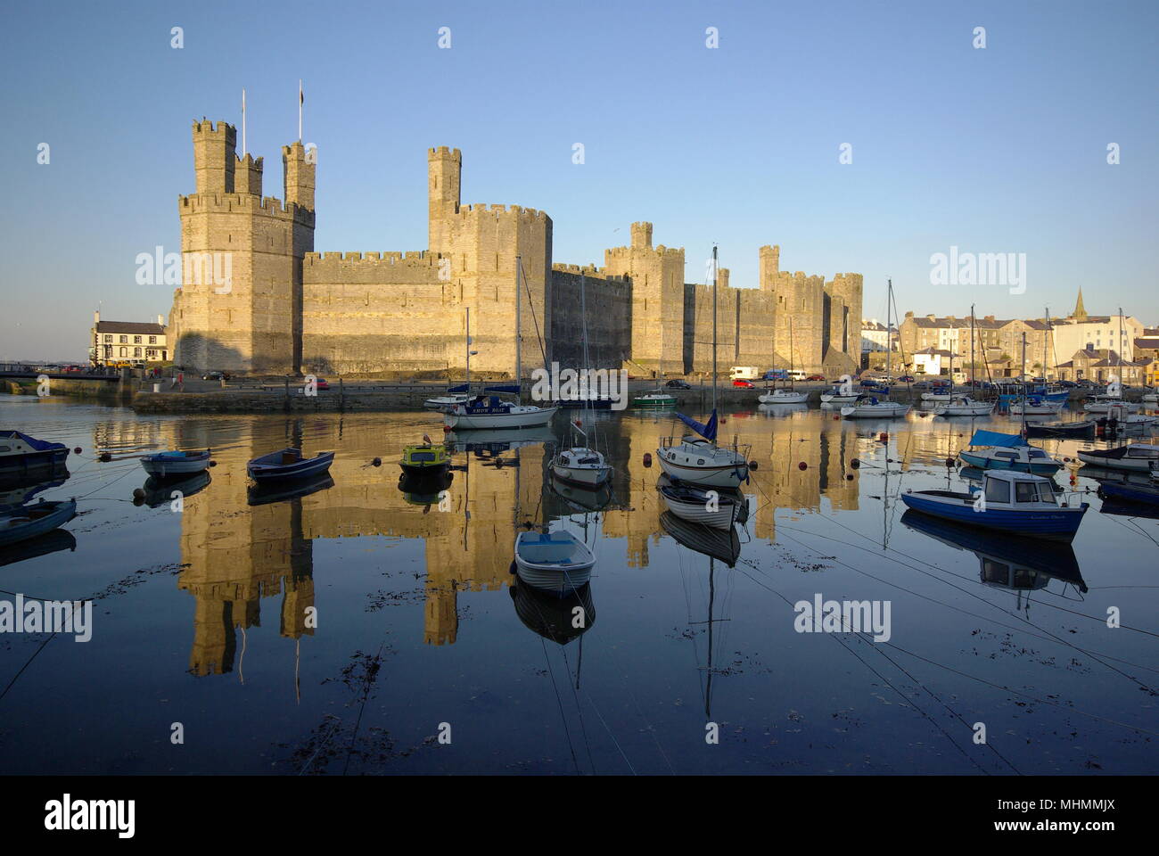 Una vista impressionante del castello di Caernarfon (Caernarvon) nel Gwynedd, Galles del Nord, con numerose barche in acqua in primo piano. Il castello fu costruito dal re inglese Edoardo i intorno al 1283, sul sito di una fortezza romana e Norman motte. Foto Stock