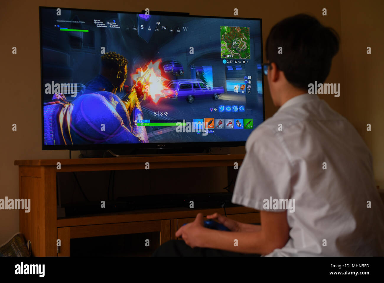 Un ragazzo adolescente gioca il colpo computer game Fortnite su un TV di grandi dimensioni su una Playstation 4 Console. Foto Stock