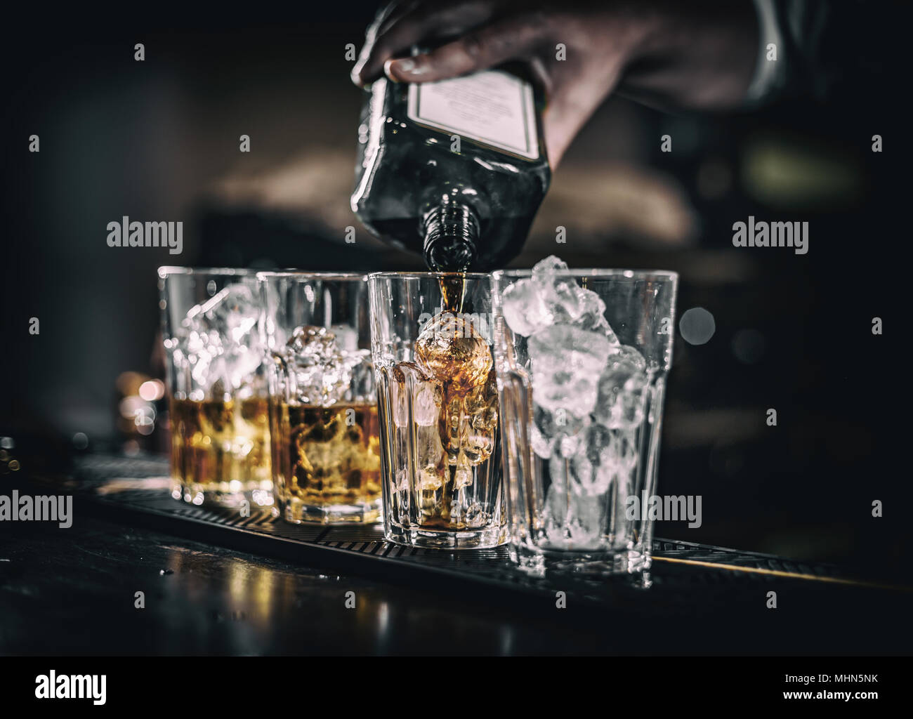 Barman versando la bevanda alcolica nei bicchieri con cubetti di ghiaccio sul bancone del bar Foto Stock