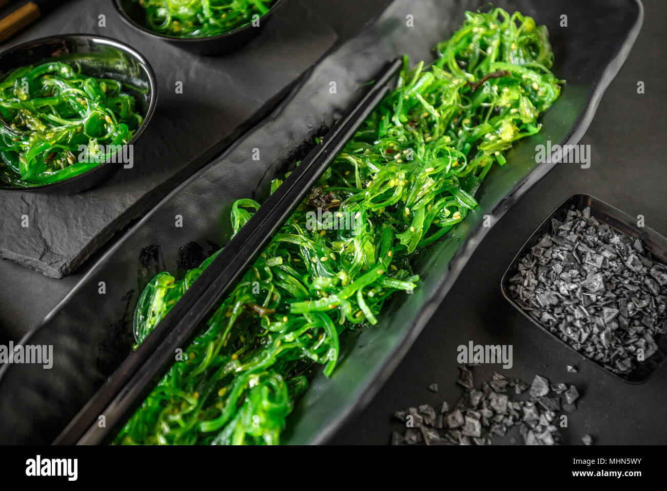 Le alghe wakame insalata servita con baguette su sfondo nero Foto Stock
