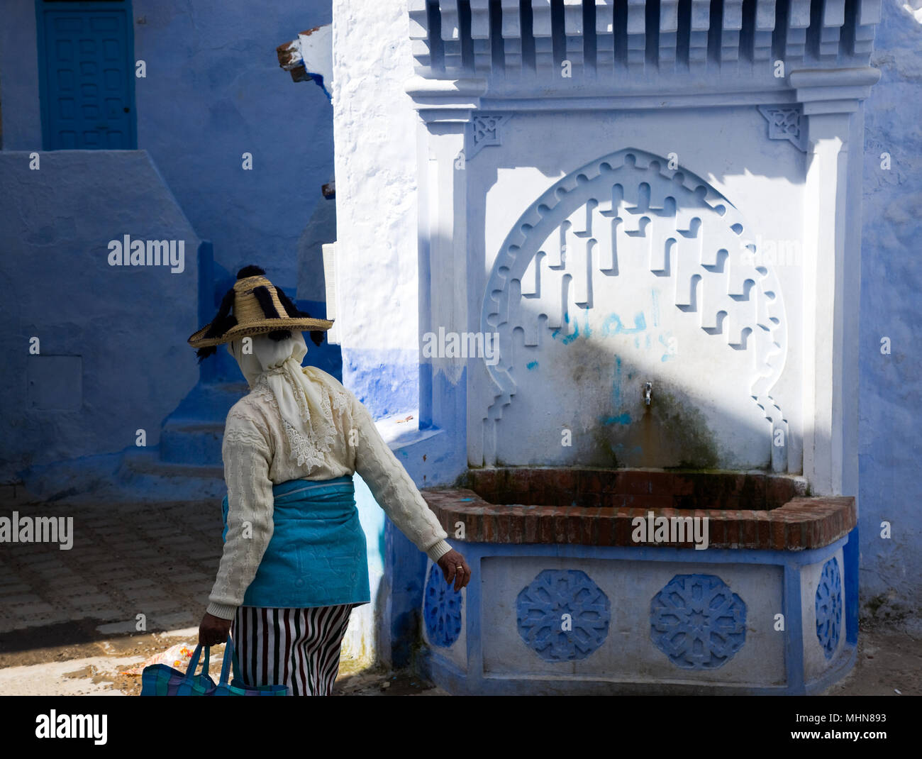 Chefchaouen, Marocco; donna in abito tradizionale dei borghi di montagna vicino a Chefchaouen (Jiblia) a fontana pubblica nella città vecchia. Foto Stock