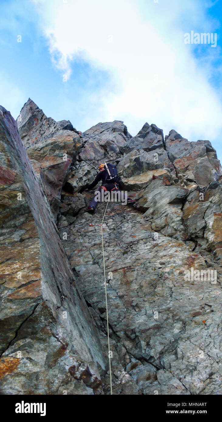 L'alpinista salendo una ripida parete di roccia sul suo modo di un alta vetta alpina Foto Stock