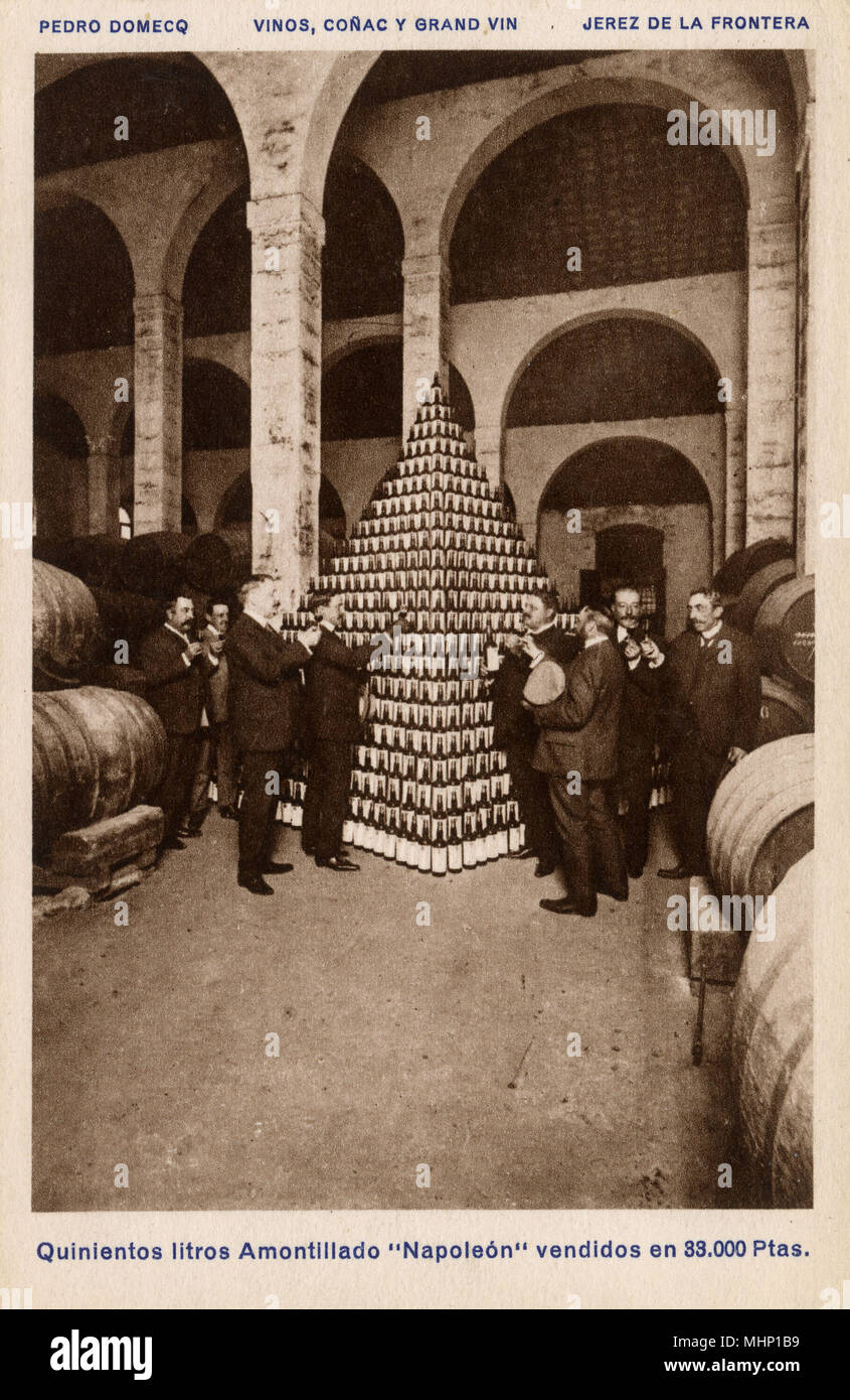 In scena la Pedro Domecq cantine, Jerez de la Frontera, Cadice, Spagna -- uomini che tengono i bicchieri di vino, con una piramide di cinque centinaia di litri di Napoleone di Sherry amontillado. Data: circa 1920s Foto Stock