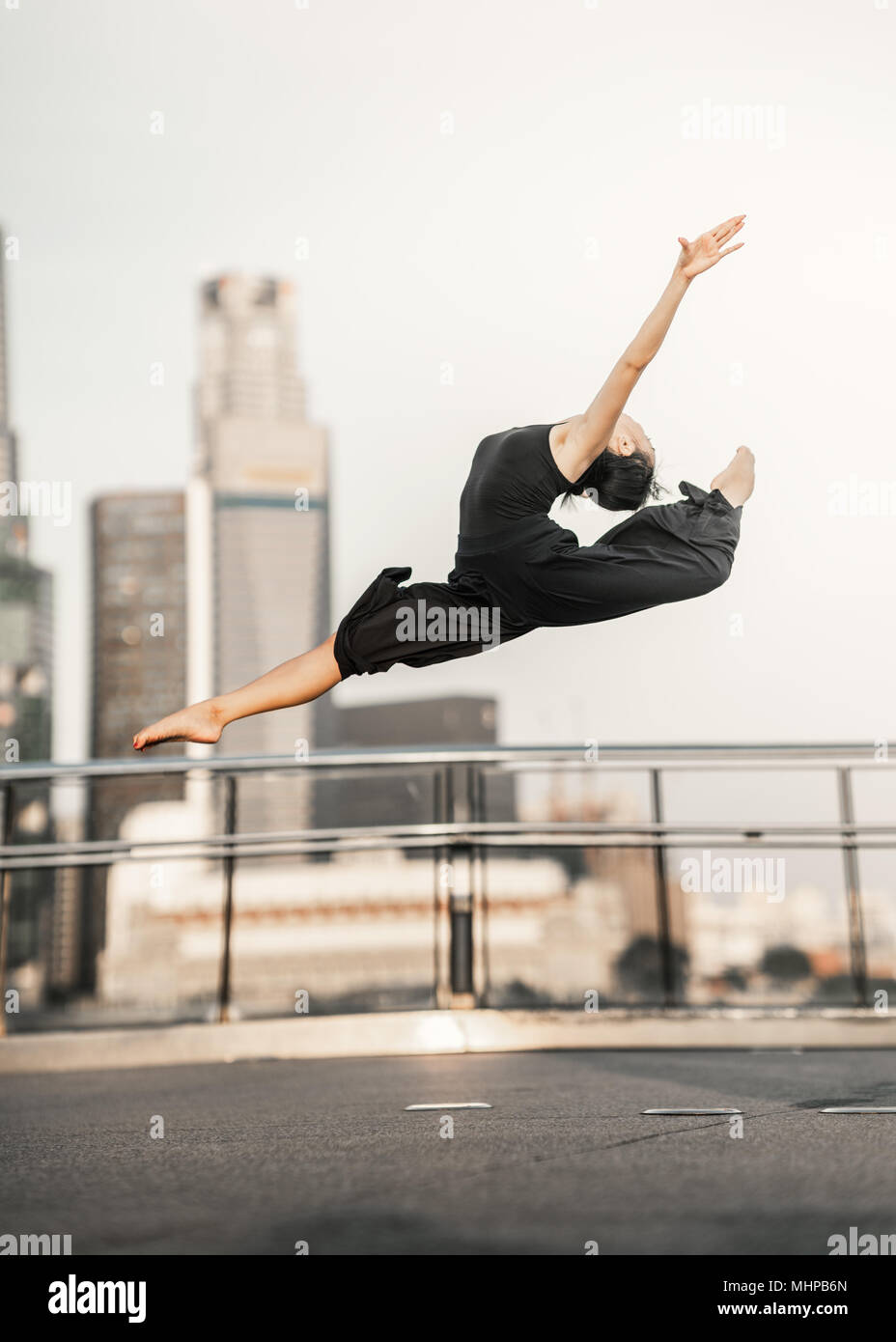 Passione... Donna giovane atleta svolge un perfetto salto in alto, su un ponte con lo sfondo dei grattacieli Foto Stock