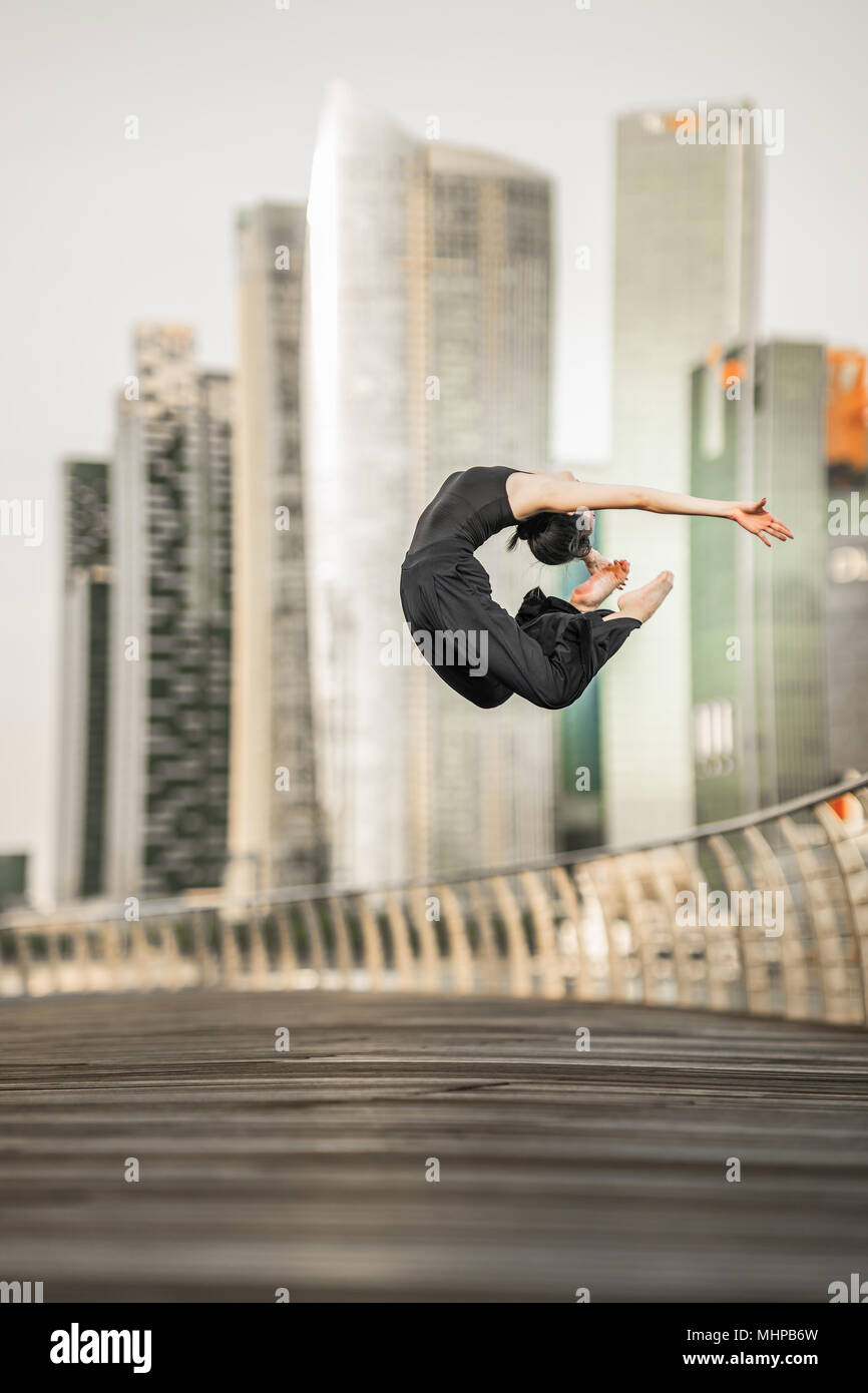 Appassionata donna giovane atleta svolge un perfetto salto in alto, su un ponte con lo sfondo dei grattacieli Foto Stock