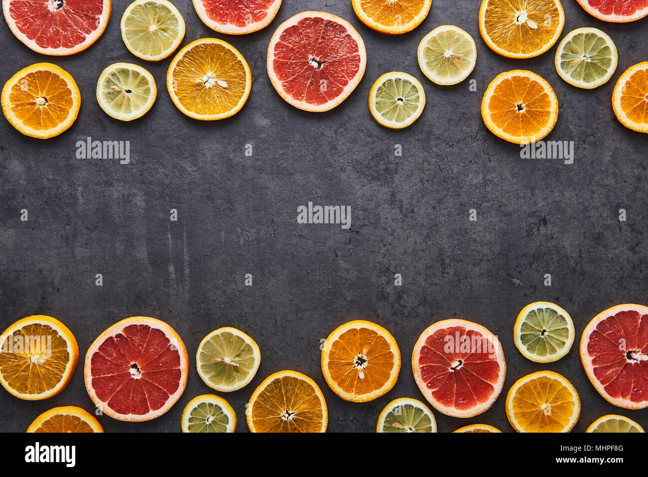 Piatto di laici agrumi modello di limone, arancia e pompelmo sulla pietra nera dello sfondo. Copia spazio in mezzo. Vista dall'alto. Foto Stock