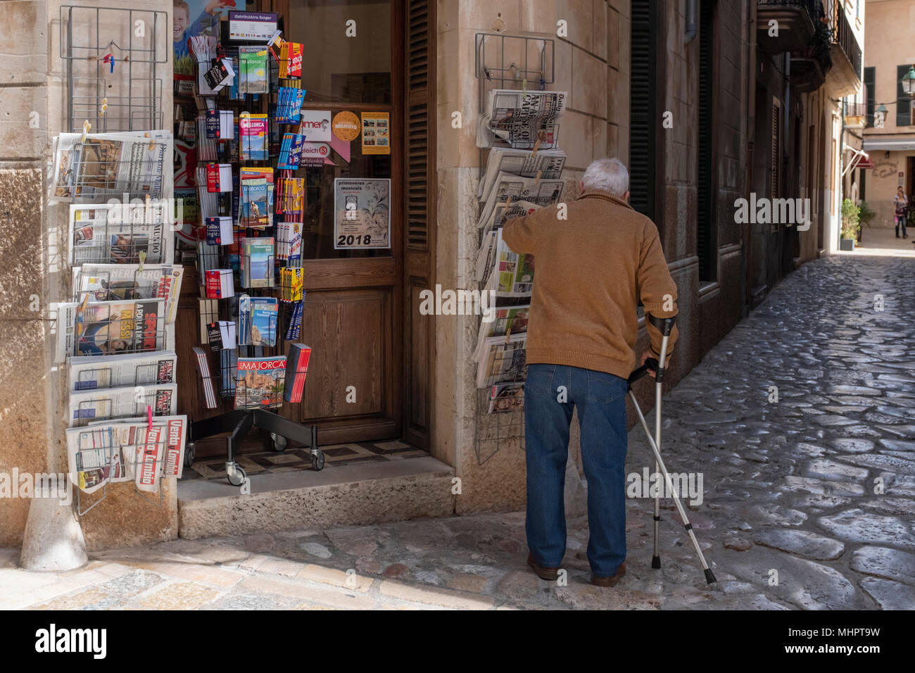 Un uomo anziano al di fuori di un negozio di giornali in Pollensa town, Mallorca, Spagna. Foto Stock
