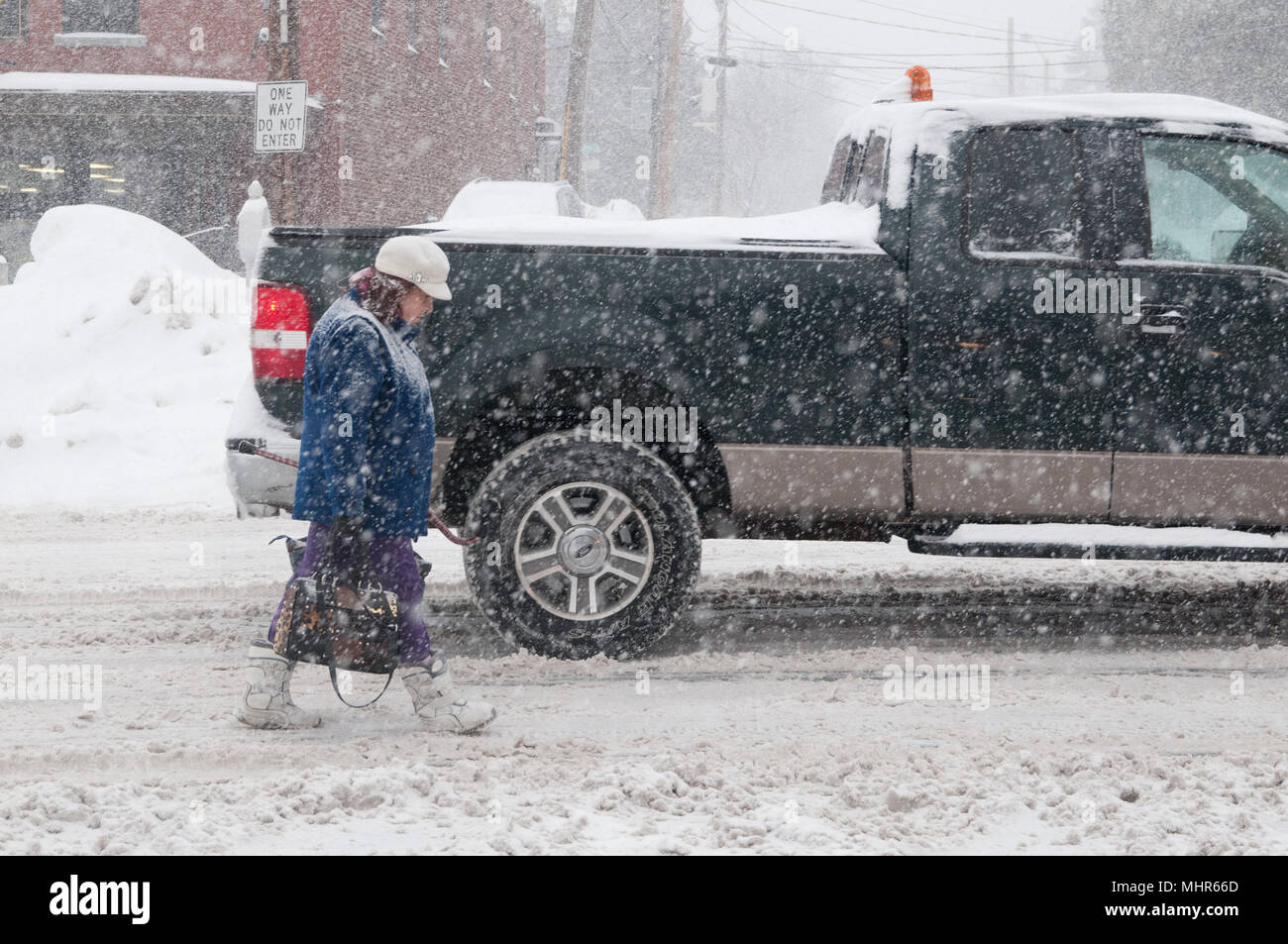 La donna a piedi in strada durante una tempesta di neve perché i marciapiedi sono coperti di neve Foto Stock