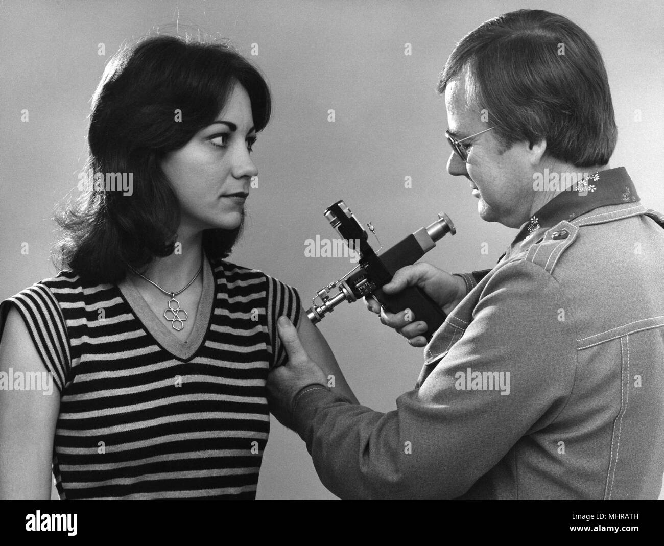 La sanità pubblica lavoratore la vaccinazione di una giovane donna con un iniettore a getto, 1976. Immagine cortesia di centri per il controllo delle malattie (CDC). () Foto Stock