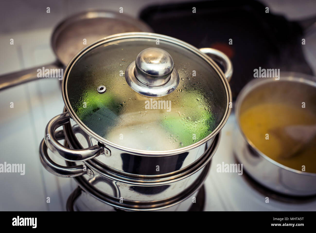 Acciaio inossidabile sistema di cottura a vapore la cottura a vapore di broccoli con pentola di zuppa di riscaldamento accanto ad essa sul piano cottura Foto Stock