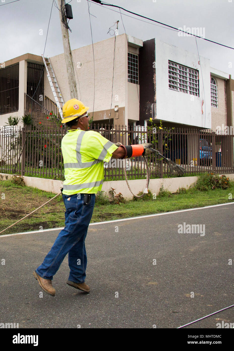 Un lavoratore di linea lancia una corda guida su un cavo esistente. Egli potrà utilizzare la fune per tirare una nuova linea attraverso la strada.il lavoro degli equipaggi di riparazione delle linee elettriche in una cima comunità in Naranjito. Come del 26 marzo 2018, oltre il 94 percento dei clienti in Puerto Rico hanno Alimentazione ripristinata. Il restante 6 per cento sono situati principalmente nelle aree montane. Nonostante il trasporto e sfide di accesso, il lavoro degli equipaggi sull isola si stanno concentrando i loro sforzi in queste aree remote, con l obiettivo di raggiungere il 95% di restauro in queste regioni entro la fine di maggio. Foto Stock