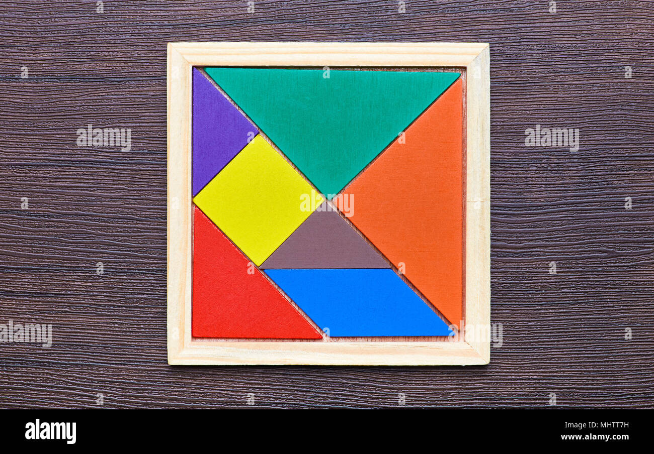 Un tangram puzzle costituito da pezzi colorati con forme geometriche, raccolti in una piazza al buio su un sfondo di legno Foto Stock