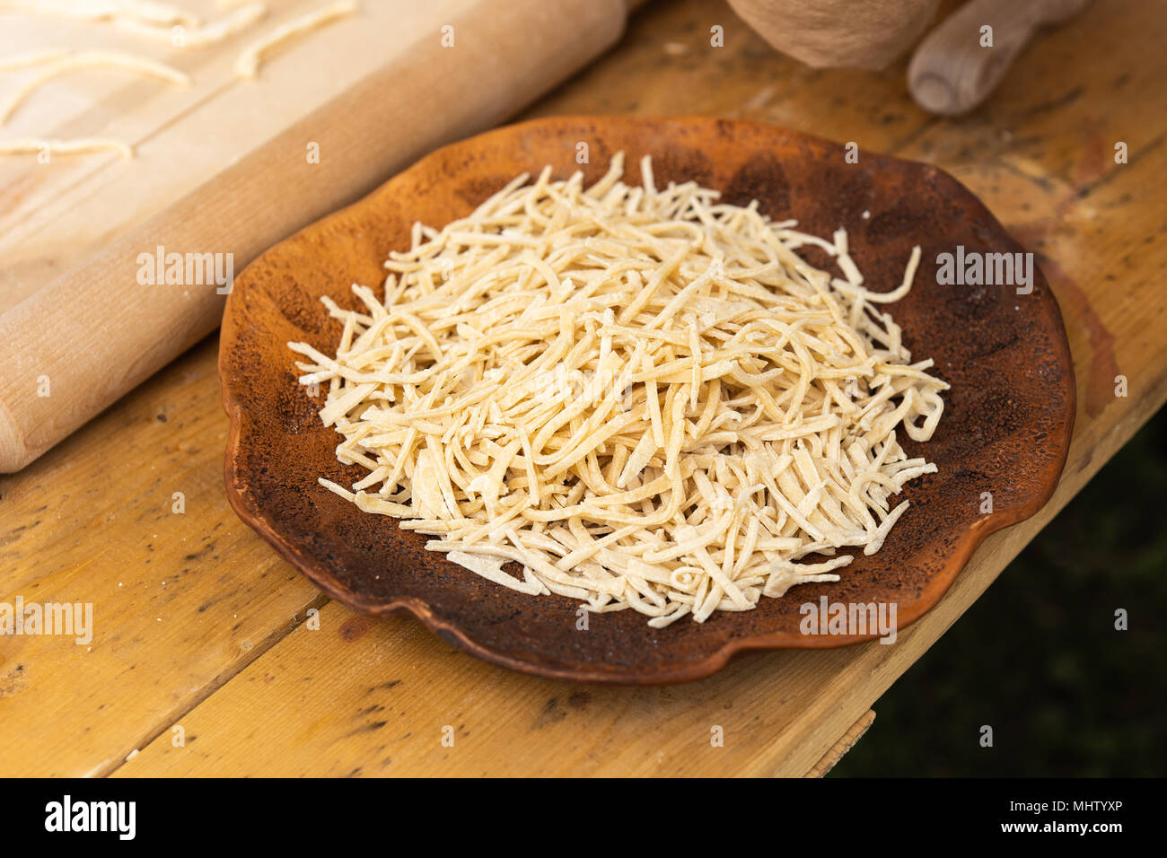 Vintage piatto di terracotta pieno di freschi a base di noodle sorge su di un tavolo di legno. Dettaglio di una cucina medievale. La preparazione di alimenti Foto Stock