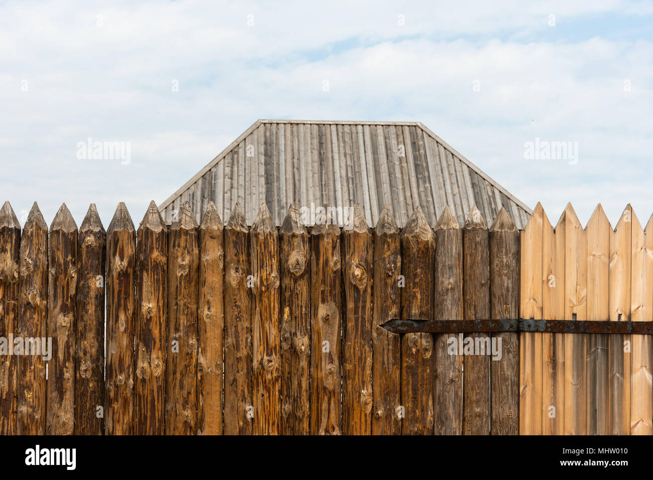 I registri di punta di un antico scherma pallido o palizzata. Un tetto in legno di un edificio che si trova dietro il recinto. Metallo arrugginito cerniera di porta. Cielo Molto nuvoloso Foto Stock