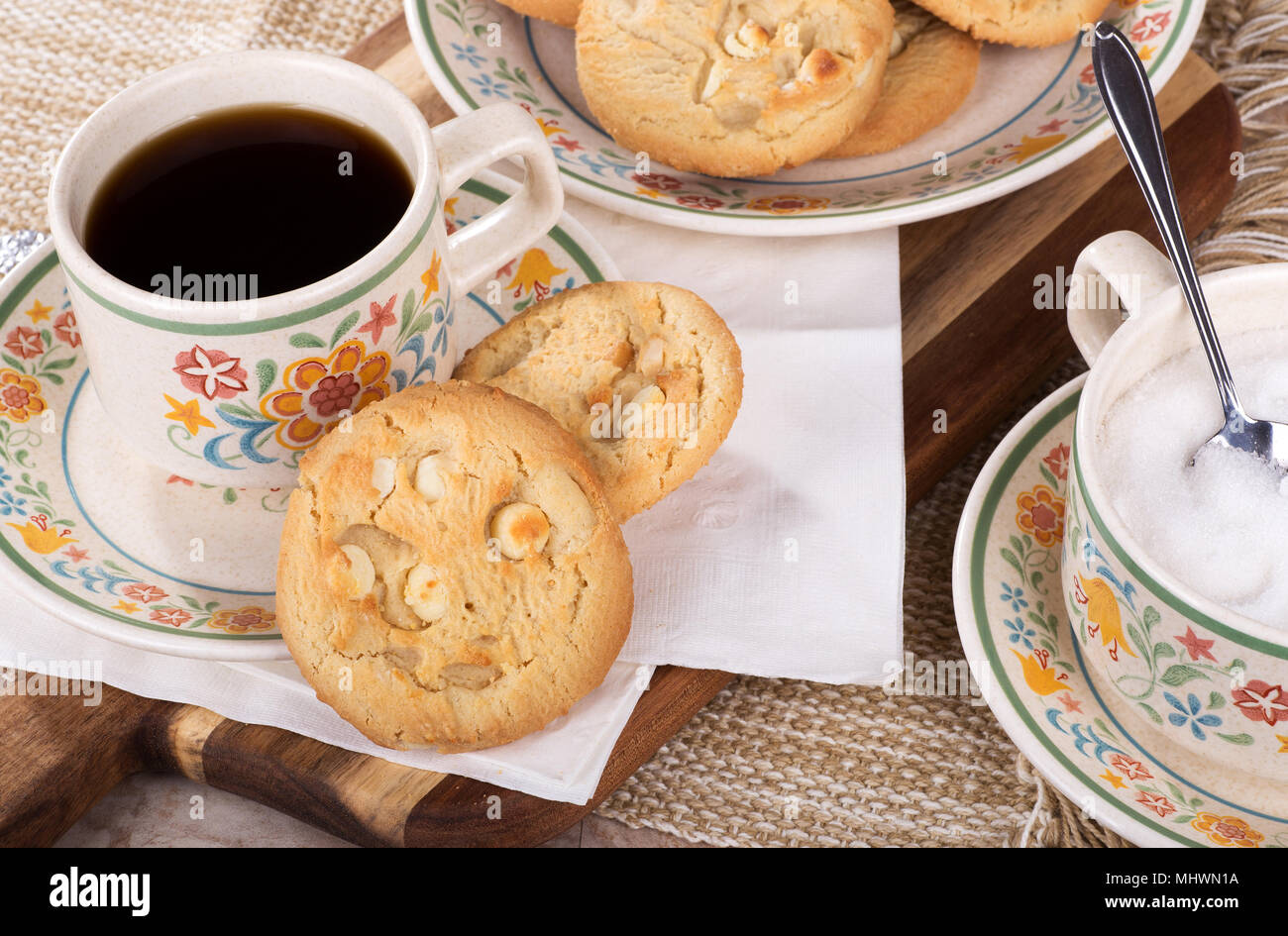Noce Macadamia cookie e tazza di caffè su una piastra con una piastra di cookie e la tazza di zucchero Foto Stock