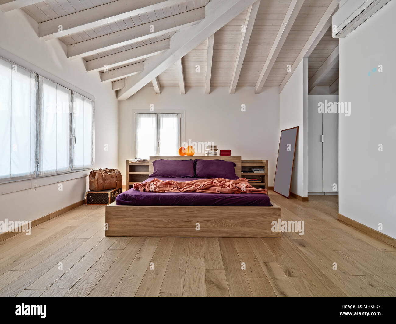 Scatti di interni di una moderna camera da letto in mansarda con letto in legno e il soffitto in legno Foto Stock