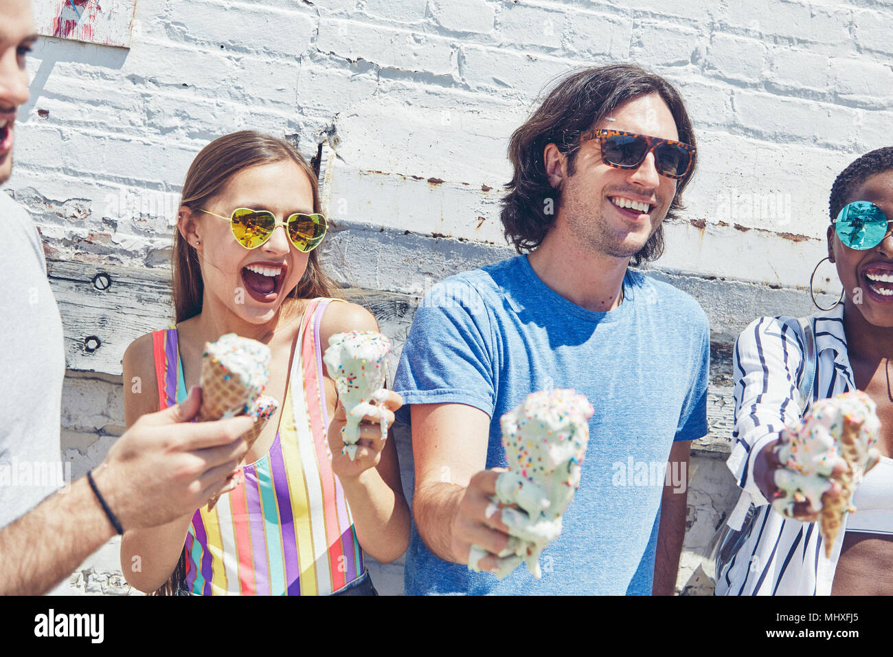 Giovani donne e uomini che tengono la fusione coni gelato, ridendo Foto Stock
