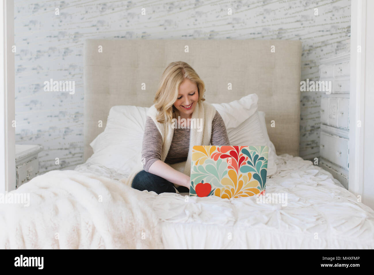 Giovane donna seduta sul letto digitando su laptop Foto Stock