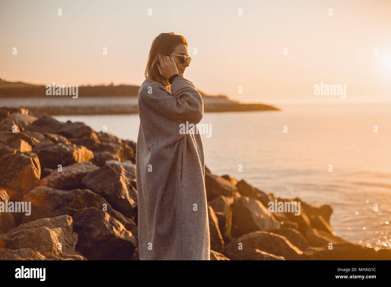 Ritratto di donna che indossa gli occhiali da sole e cappotto in piedi sulle rocce che guarda lontano in mare, Odessa, Odeska, Oblast di Ucraina Foto Stock